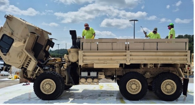 Wellington technicians stand on beige military cargo truck outdoors